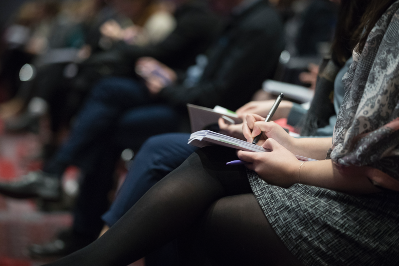 A woman writing in a notebook at a conference