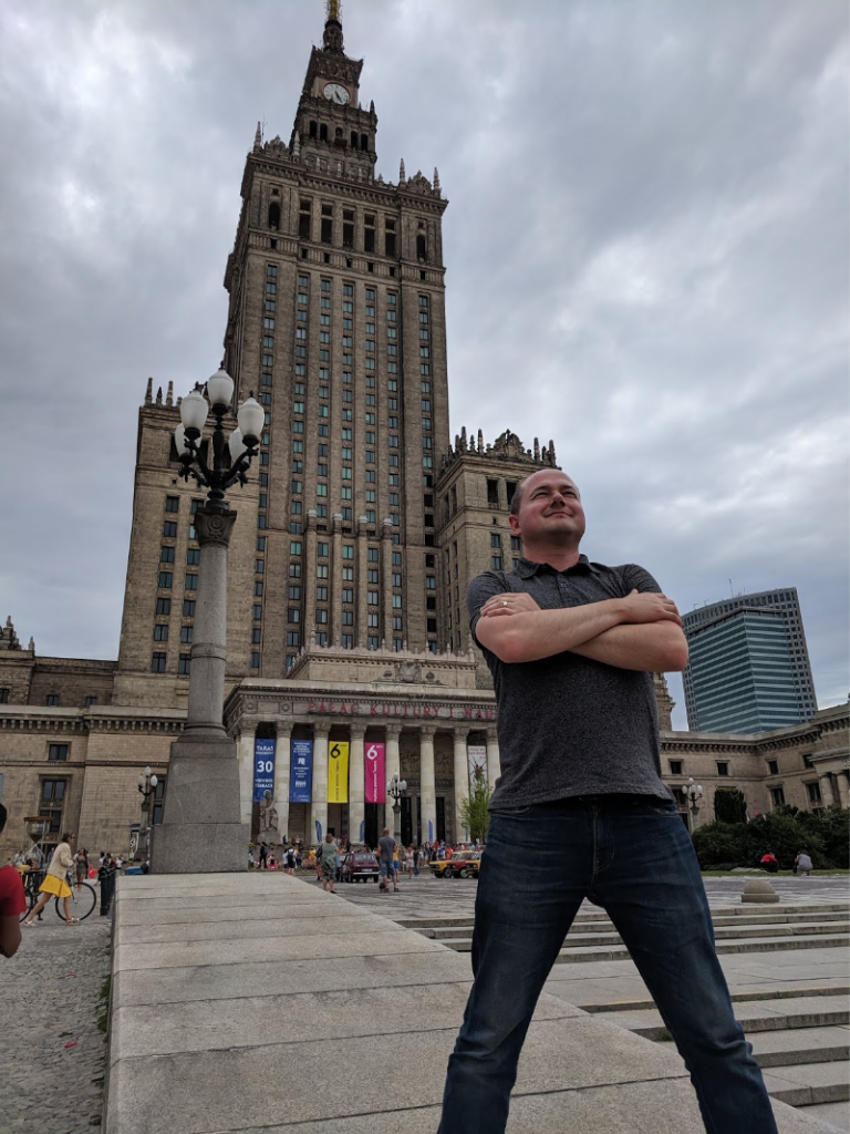 Sean stands with arms crossed in front of the Palace of Culture and Science in Warsaw, Poland.