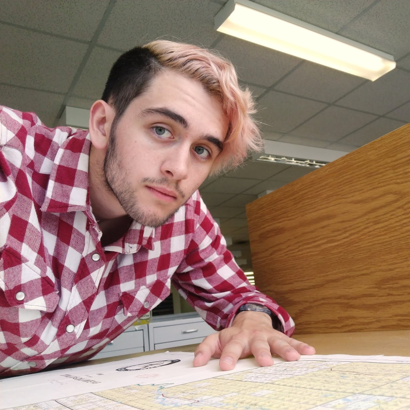 Alex leaning over a map, taking a selfie in the Maps Collection.