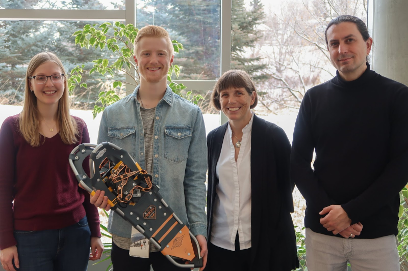 Braeden stands holding snowshoes next to two library staff members and a professor.