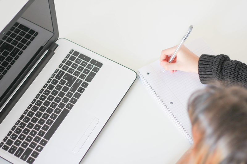 Woman taking notes beside a laptop