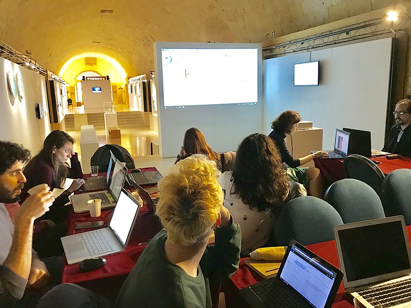 A group of people with laptops sitting together with a projector.