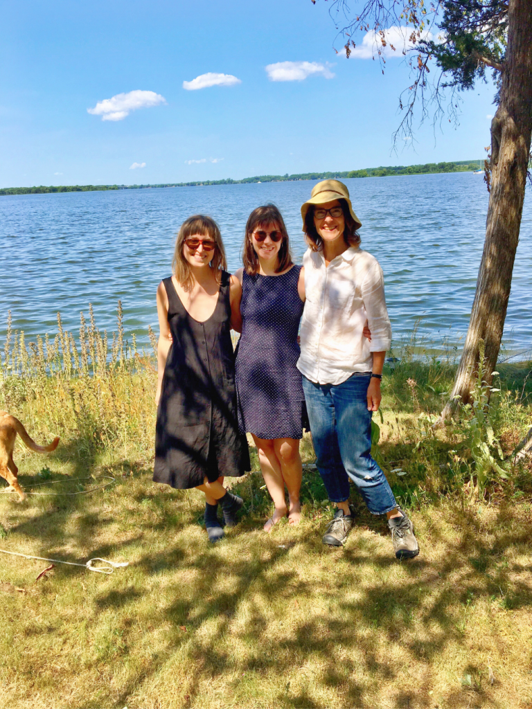 Katie, Sophie and Katherine smile for the camera while standing on a grassy waterfront.