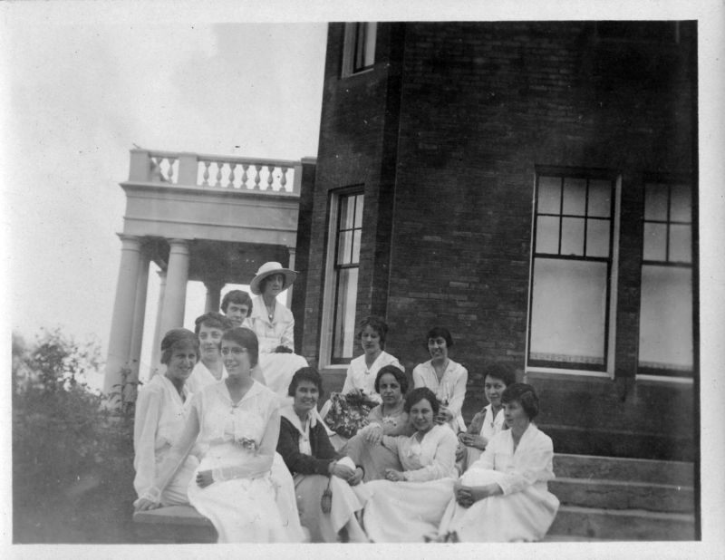 A group of women sit on the steps outside a University Building.