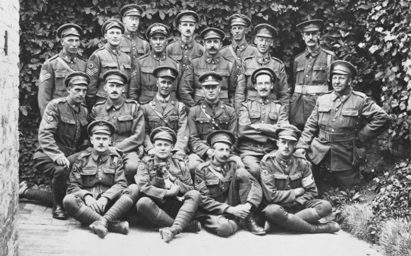 Group of soldiers posing for together in front of shrubs.