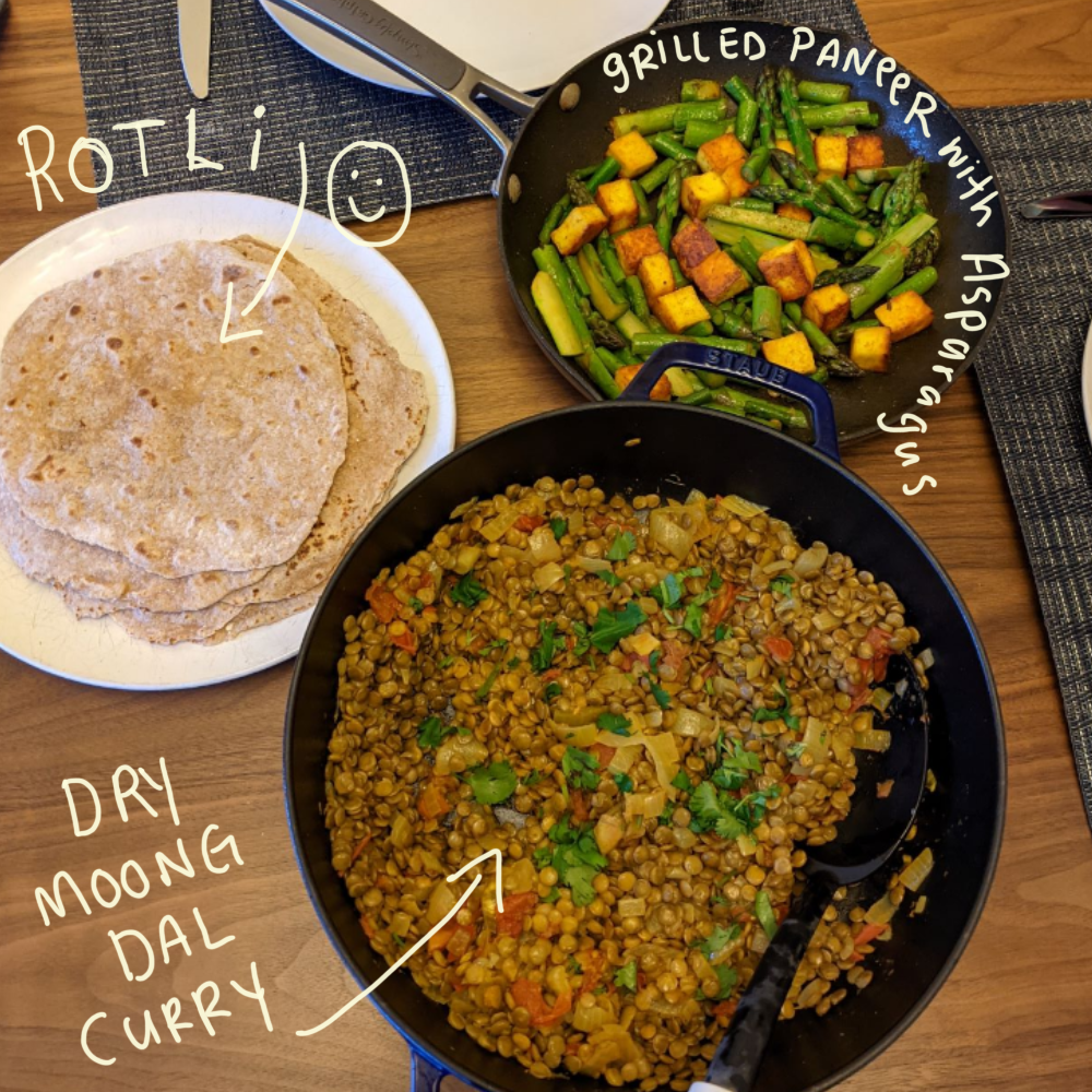Image of a table with rotli, grilled paneer with asparagus, and Dry Moong Dal Curry. Recipes from A Spicy Touch by Noorbanu Nimji. 