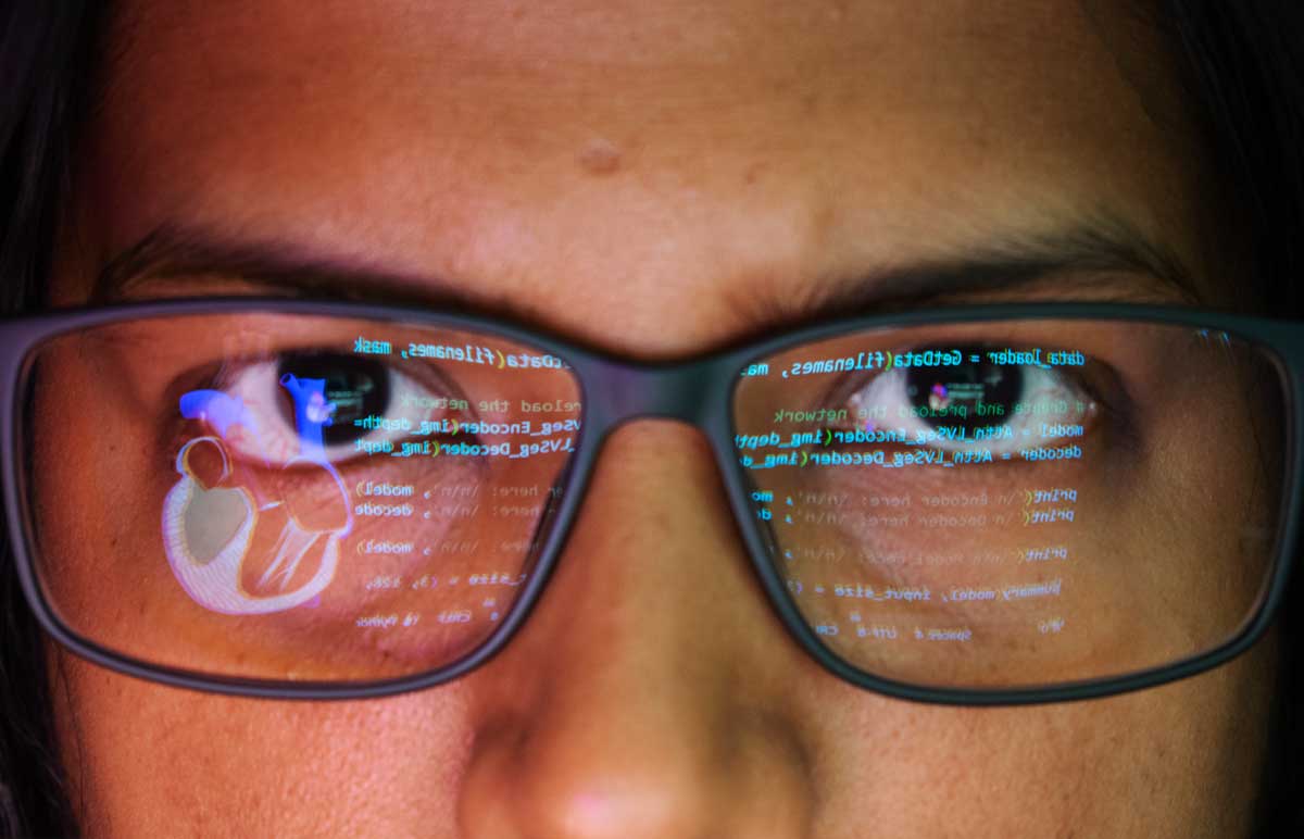 Close-up of a face wearing glasses. Focus on the glasses - reflecting lines of code on one side, a human heart on the other.